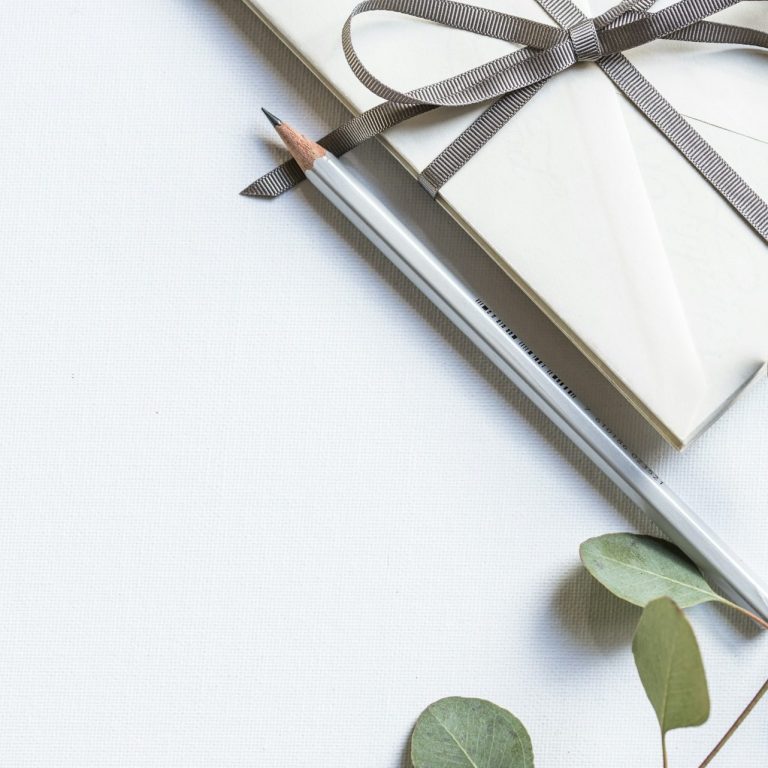 Briefumschlag mit grauer Schleife daneben ein Bleistift