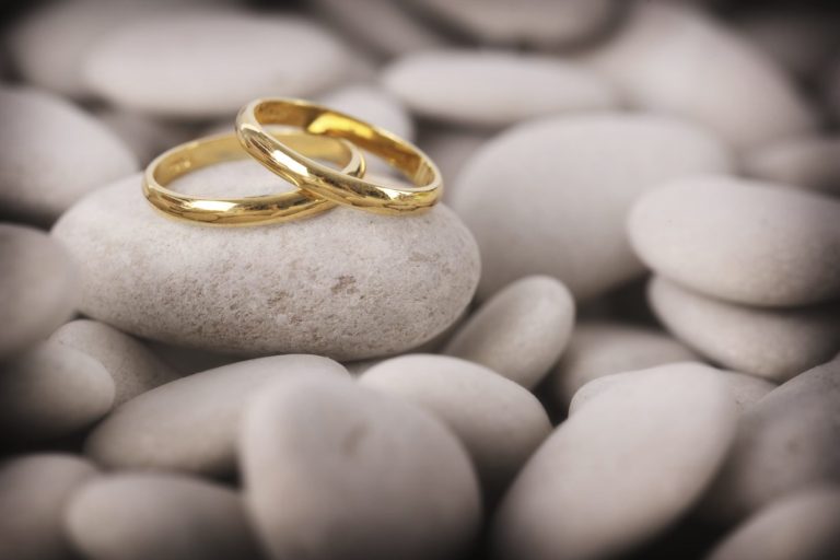 Zwei goldene Ringe liegen auf hellen Steinen