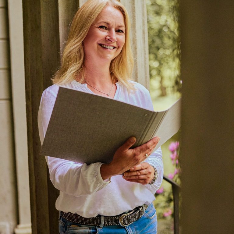 Blonde Frau mit Redner-Mappe lehnt an einer Säule