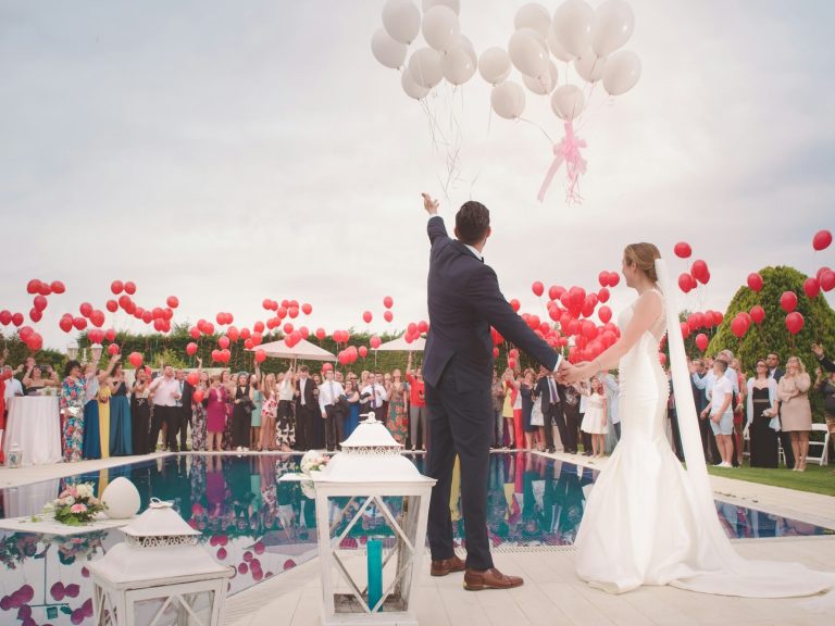 Brautpaar an einem Pool mit vielen Gästen und Luftballons